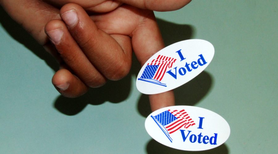 A child's hand is seen with two "I voted" stickers attached to his pointer finger.